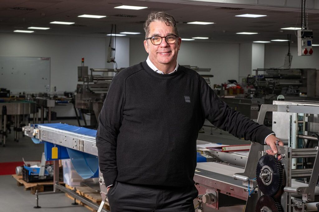 A man stands beside a conveyor belt in a factory, overseeing the production process.