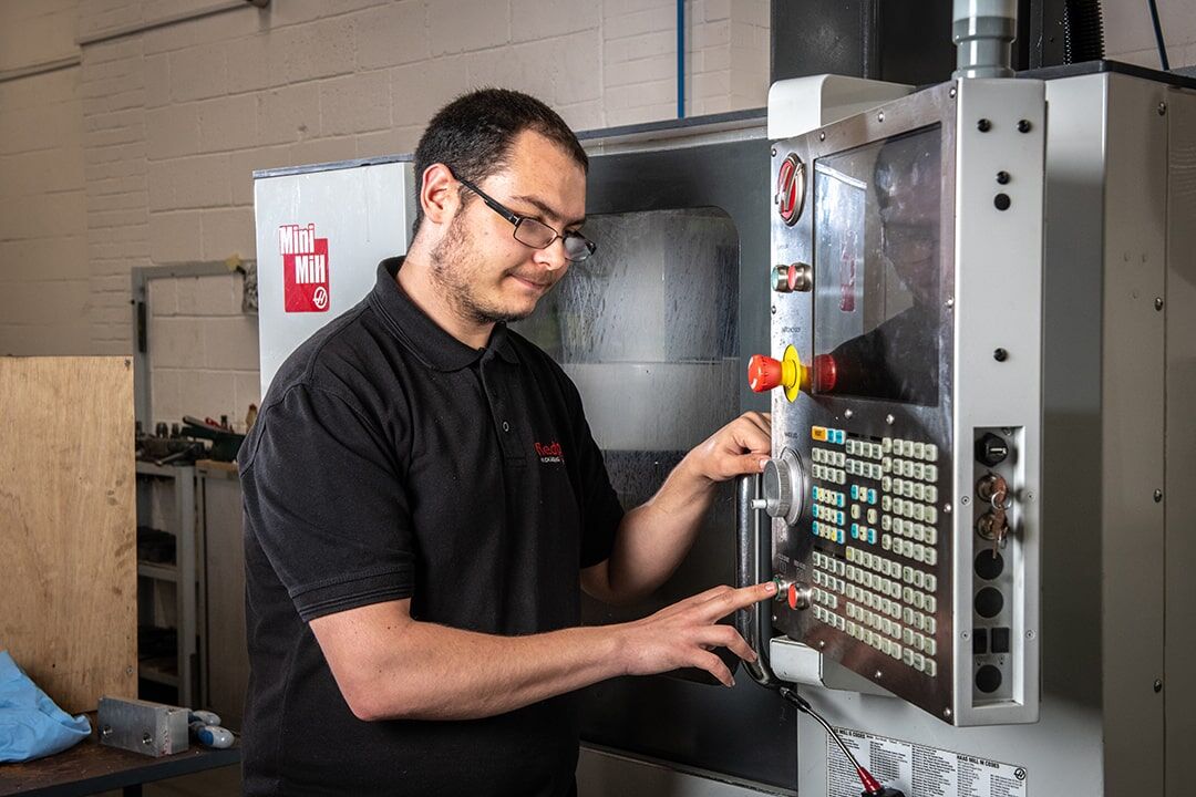 A man in a black shirt operates a machine, focused on his task in a well-lit workshop environment.