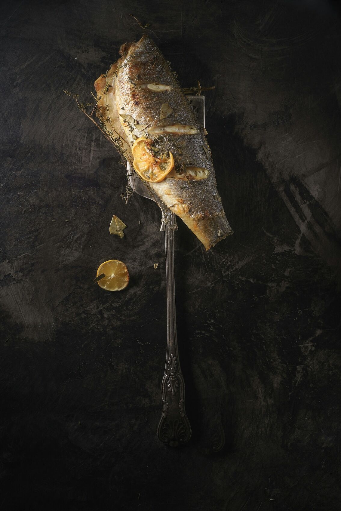 A fish on a fork, elegantly served with slices of lemon, highlighting a delicious seafood dish.