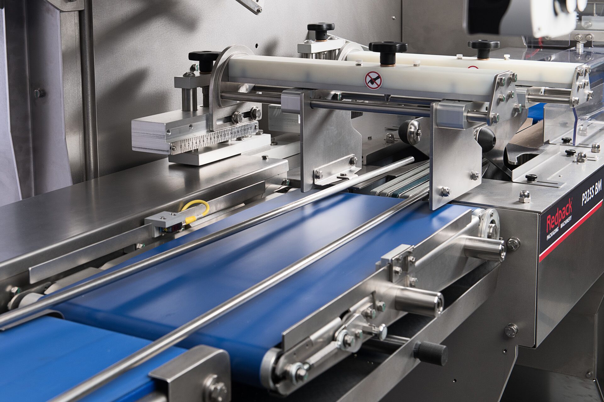 A conveyor belt transports a blue tray being manufactured by a machine in an industrial environment.