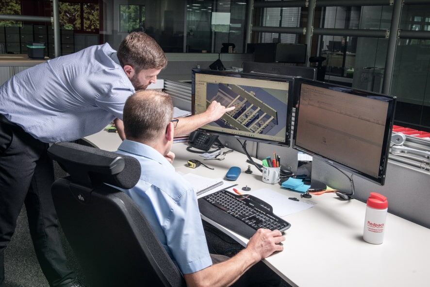 Two men collaborating on a computer in a modern office setting, focused on their work and sharing ideas.