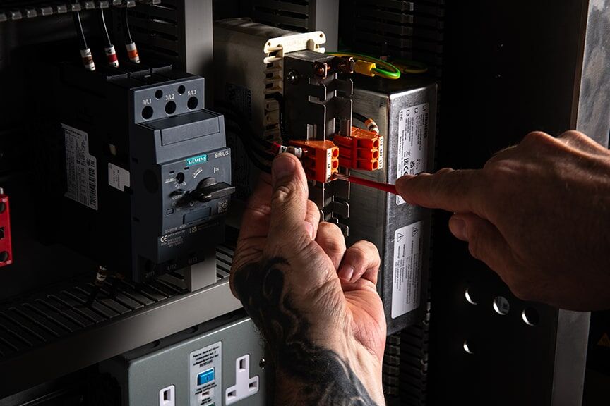 A technician works diligently on an electrical panel, managing wires and equipment for optimal performance.